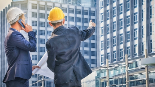 two men in hard hats pointing to a building 